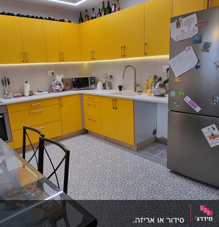 מטבח עם ארונות צהובים, מקרר עם מגנטים, כיור וברז